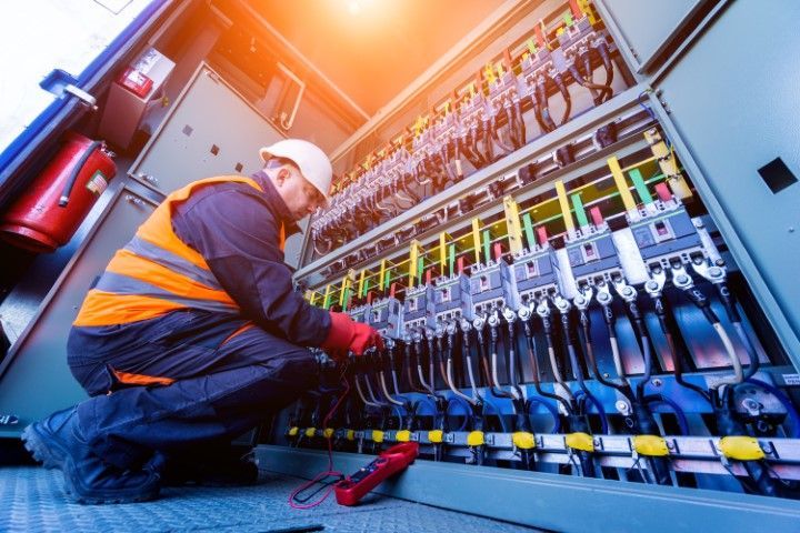 Worker in orange shirt inspects electrical wiring inside a wooden construction frame.