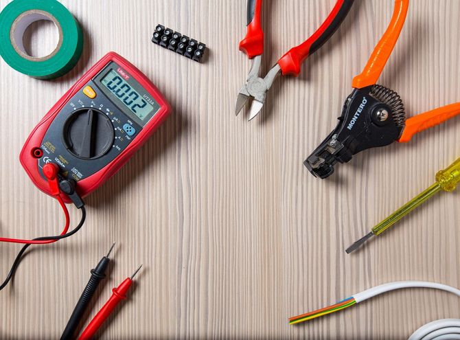 Multimeter, wire strippers, pliers, screwdriver, tape, and cables on a wooden workbench