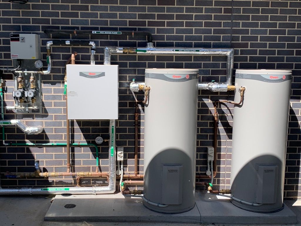 Outdoor water heater system with two cylindrical tanks, pipes, and control panel against a brick wall. — All Stars Plumbing In Albion Park, NSW