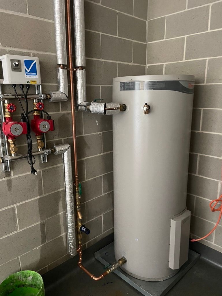 A cylindrical hot water heater with copper pipes on a gray brick wall. — All Stars Plumbing In Barrack Heights, NSW