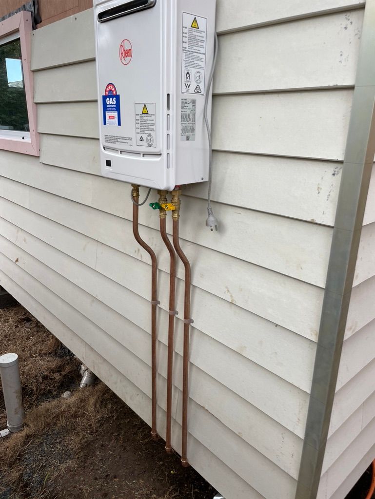 A white water heater mounted on a light beige wooden wall with copper pipes. — All Stars Plumbing In Woonona, NSW