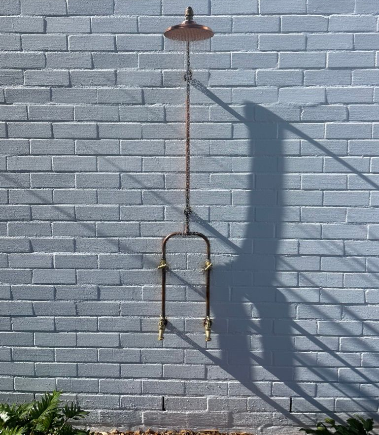 Outdoor shower fixture against a painted brick wall; copper color with rain shower head. — All Stars Plumbing In Dapto, NSW