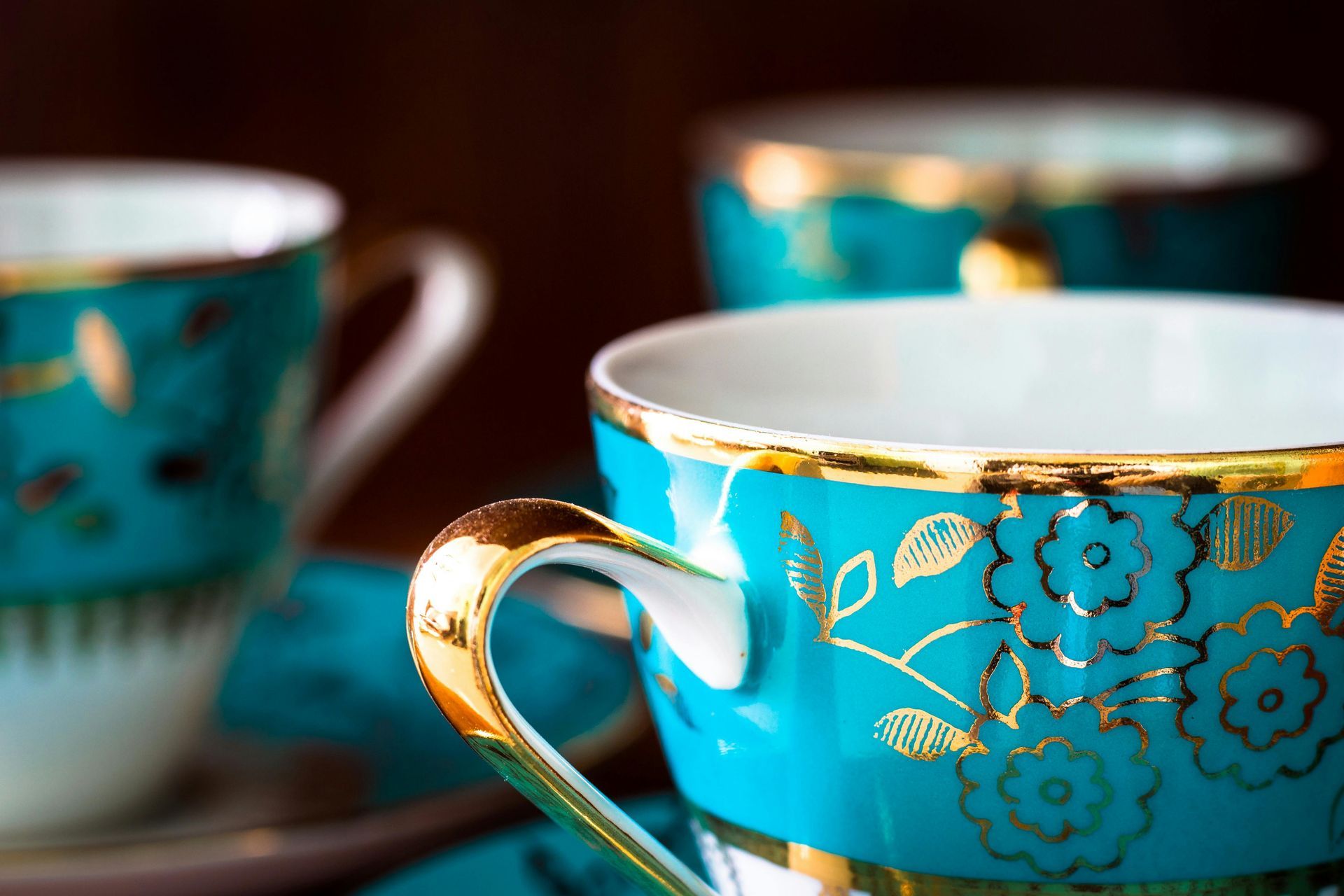 Teal teacups with gold trim and floral designs, against a dark background.