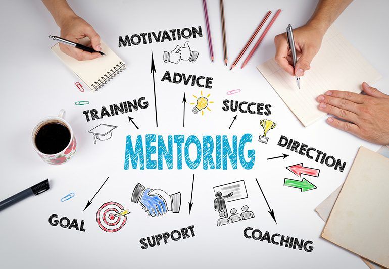 Iemand zit aan een tafel met een kop koffie en een notitieboekje met het woord mentoring erop geschreven.