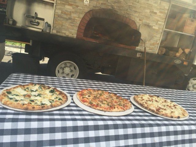 Three pizzas are sitting on a checkered table cloth