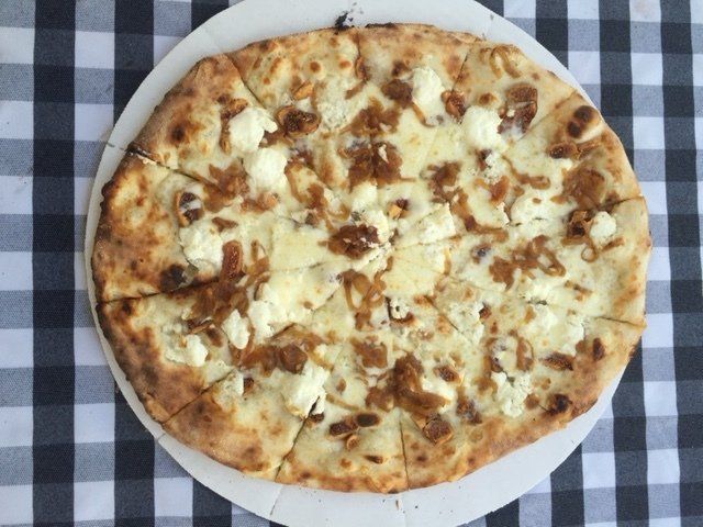A pizza is sitting on a white plate on a checkered table cloth.
