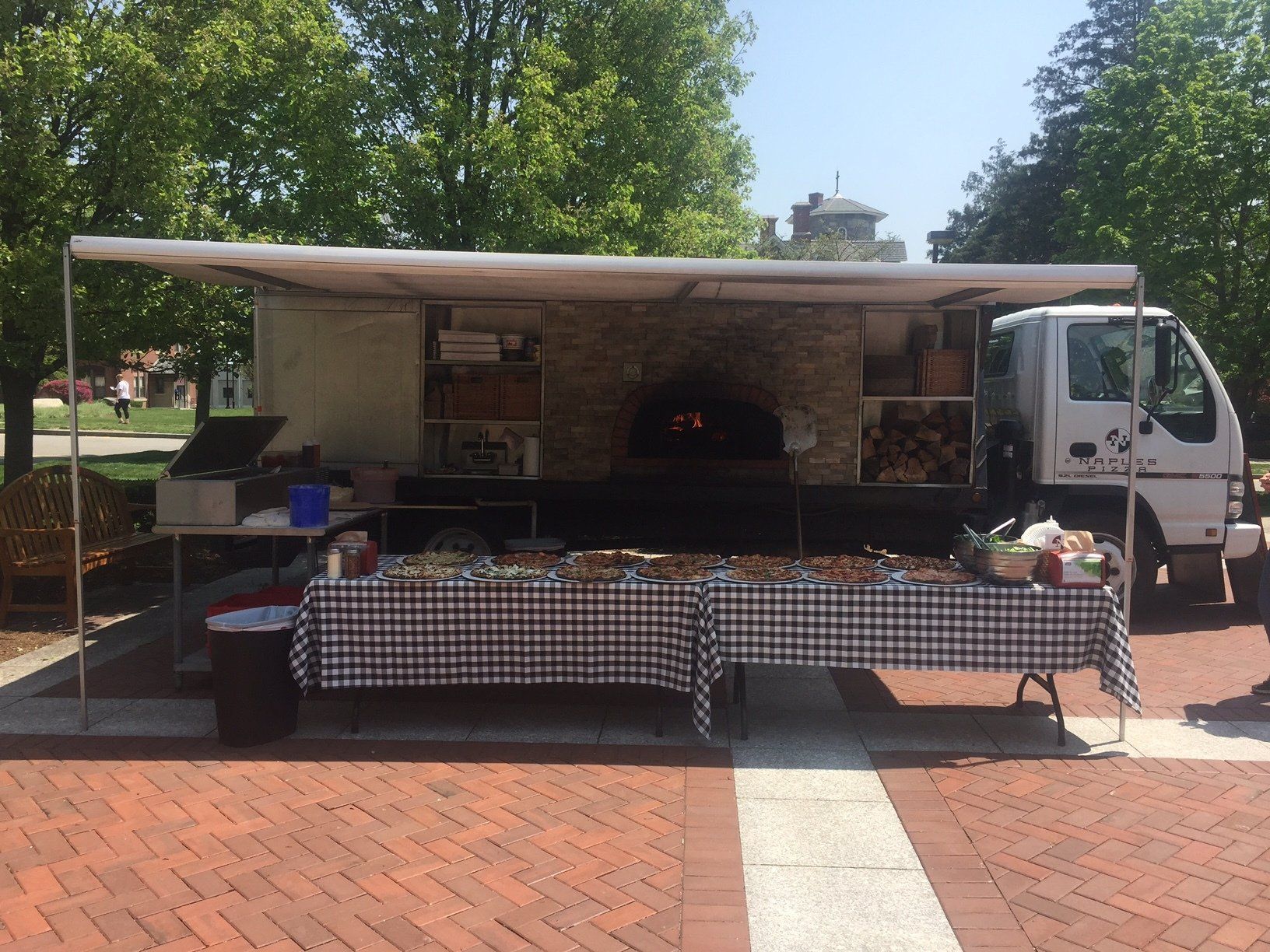 A food truck is parked on a brick sidewalk with tables in front of it.