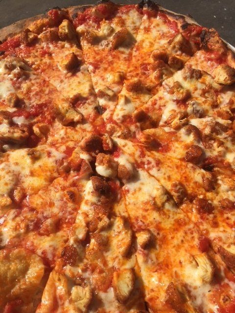 A pizza with chicken and sausage on it is sitting on a table.