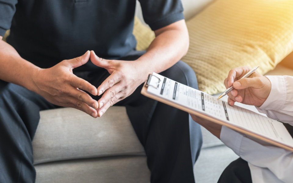 Person seated on a couch speaks with a therapist taking notes on a clipboard