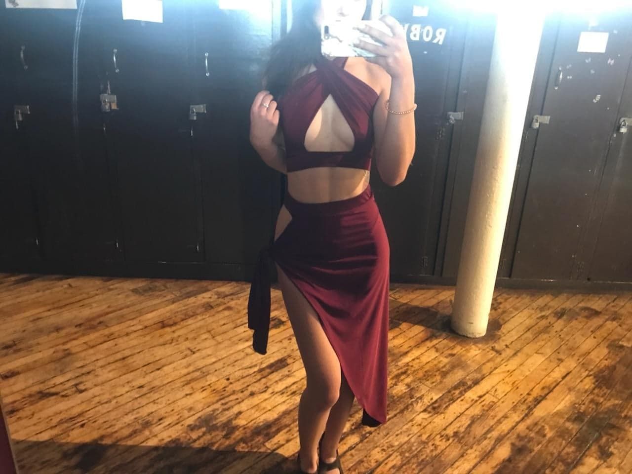 A woman in a red dress is taking a selfie in a locker room.