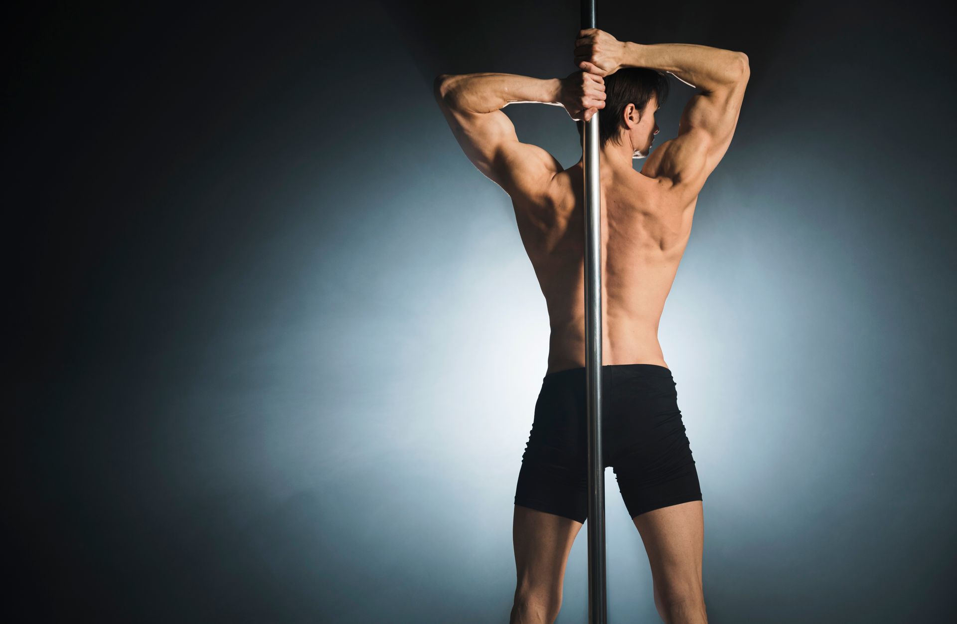 A shirtless man is standing next to a pole.