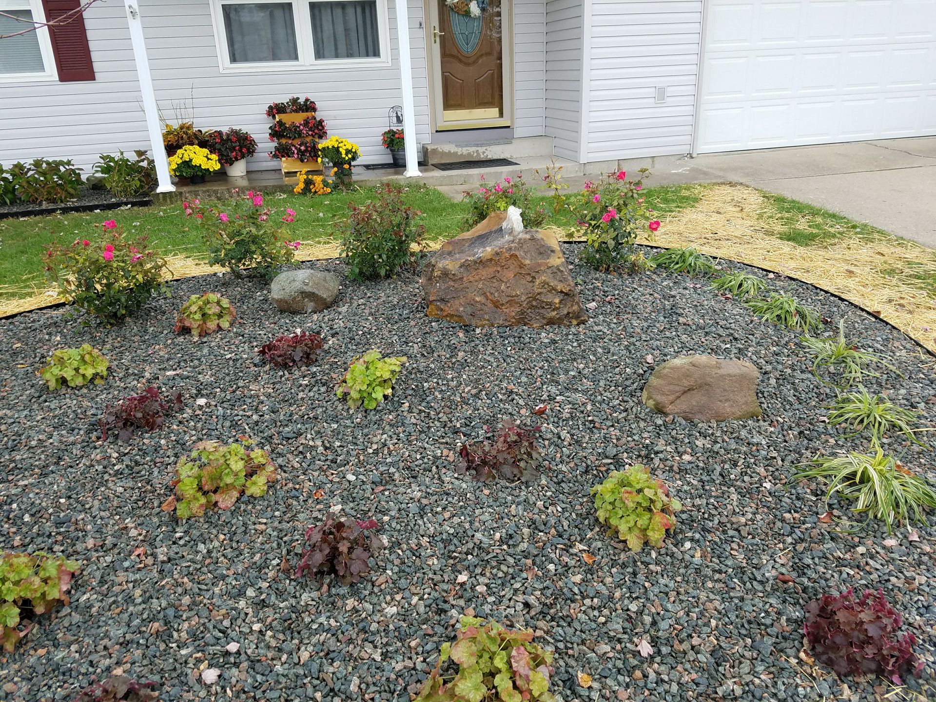 A gravel garden in front of a house with flowers and rocks.