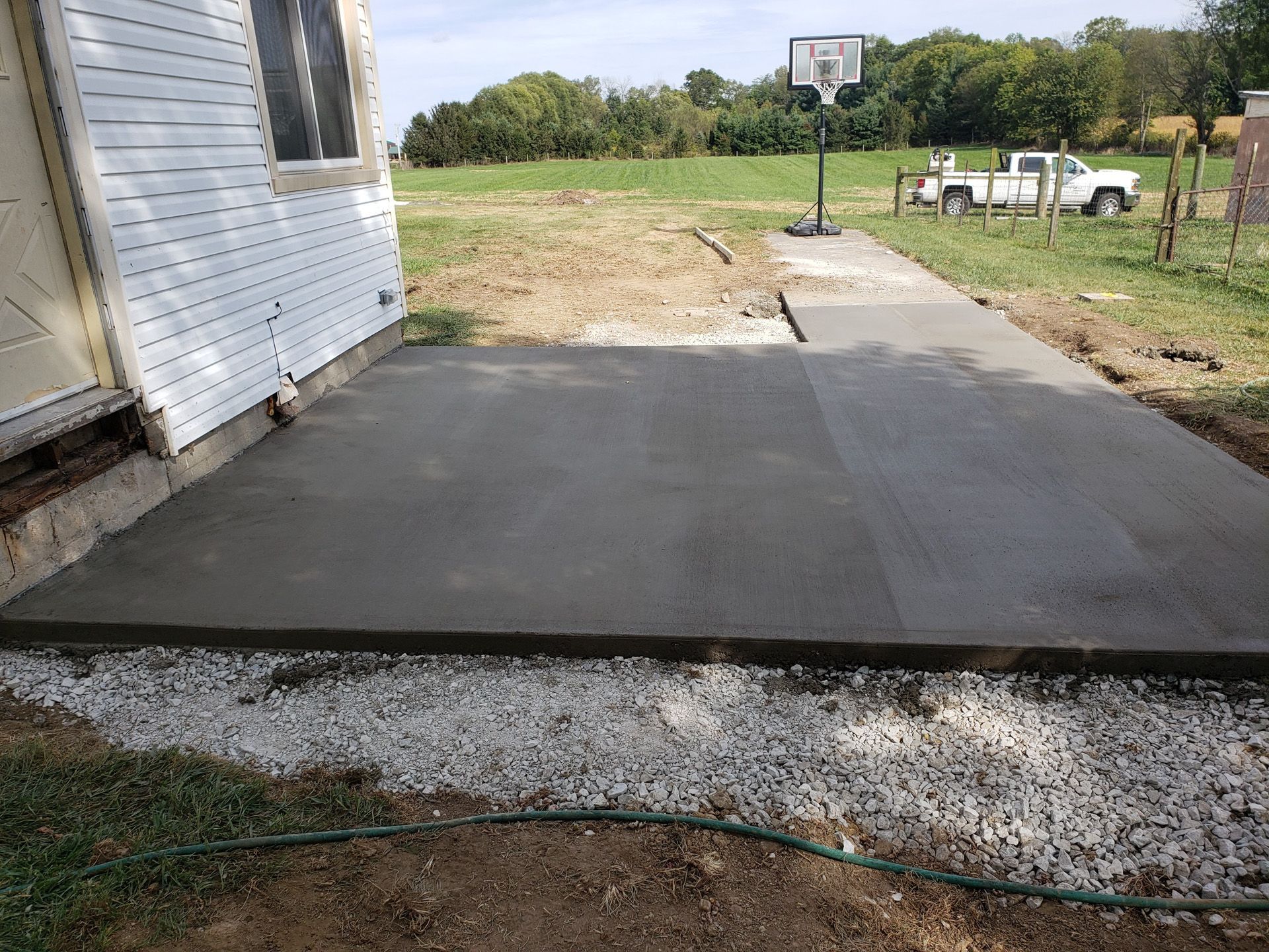 A concrete walkway is being built in front of a house with a basketball hoop in the background.