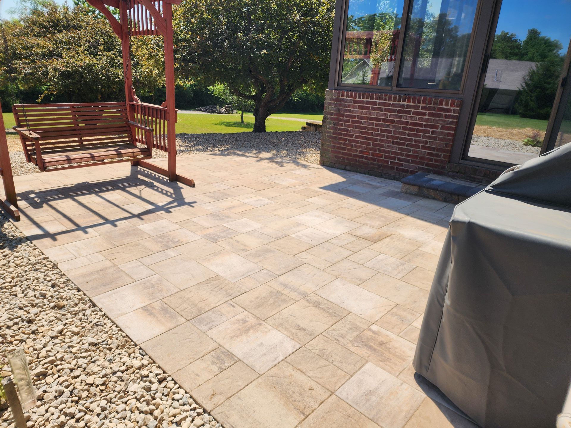 A patio with a swing and a grill in front of a brick building.