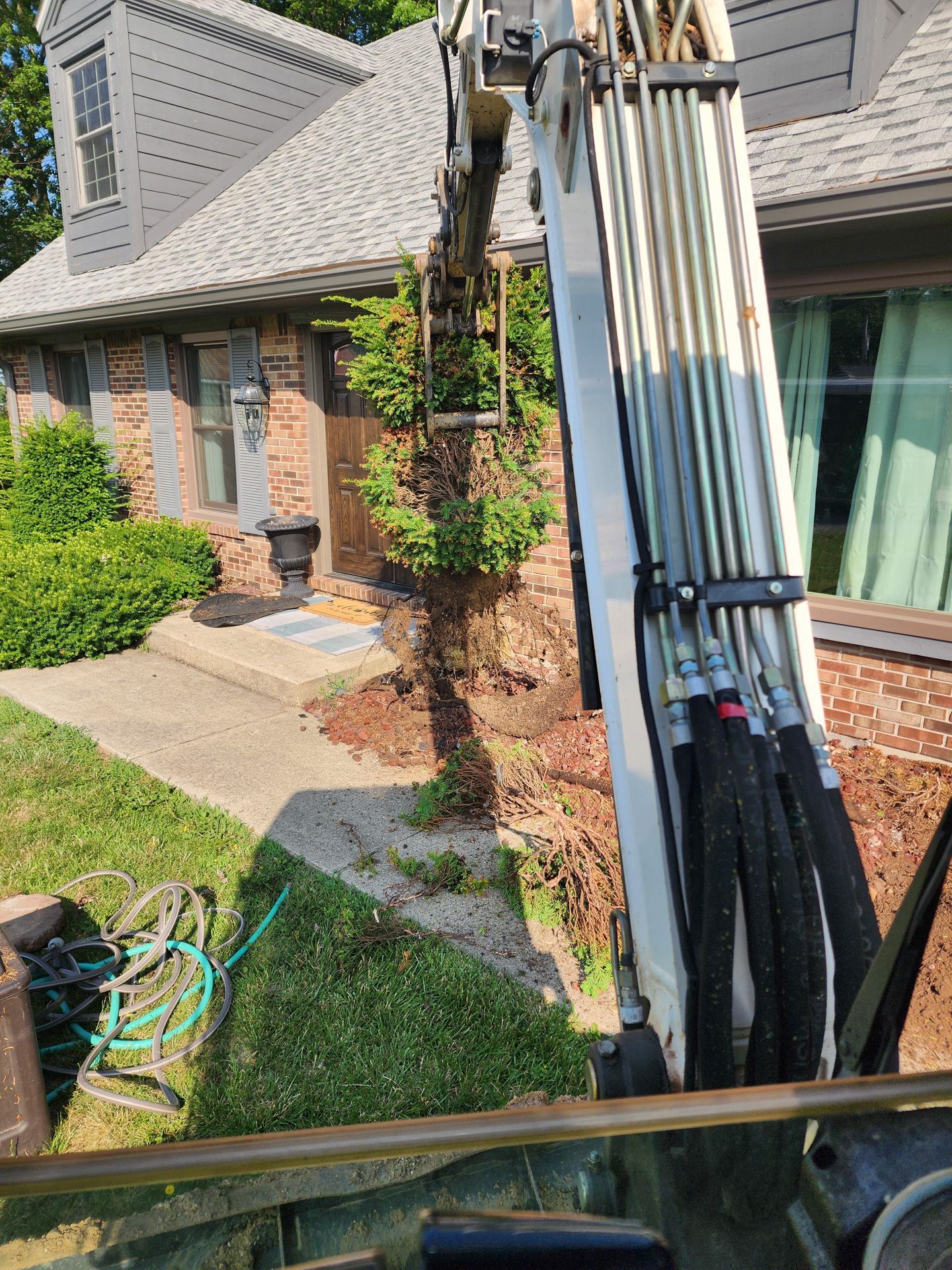 A large excavator is digging a hole in the ground in front of a house.