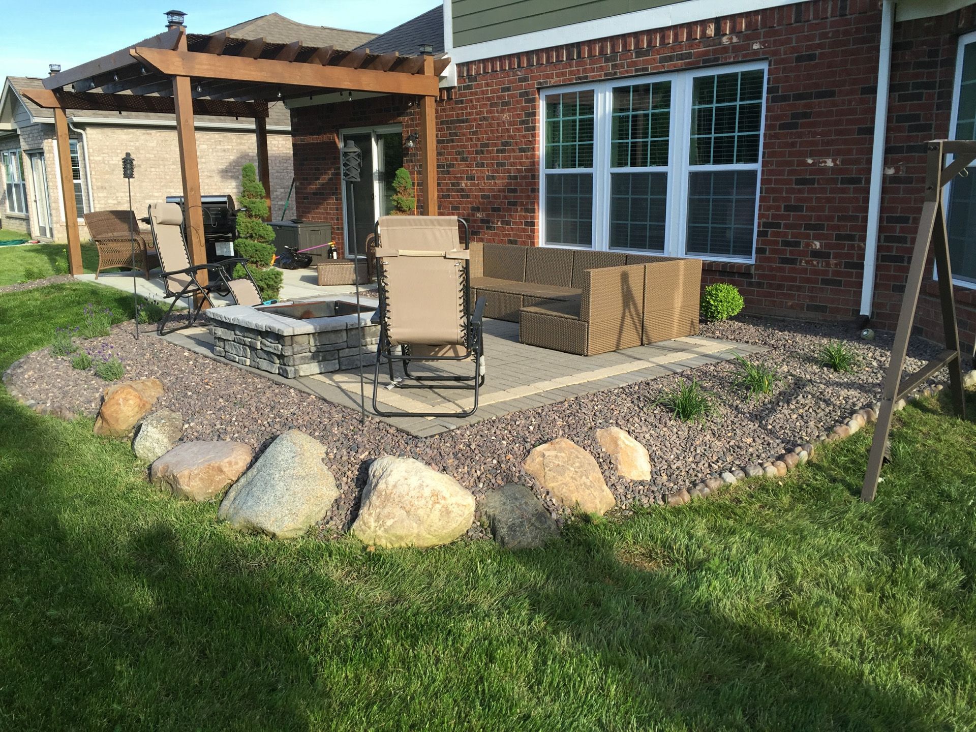 A patio with a pergola and chairs in front of a brick house.
