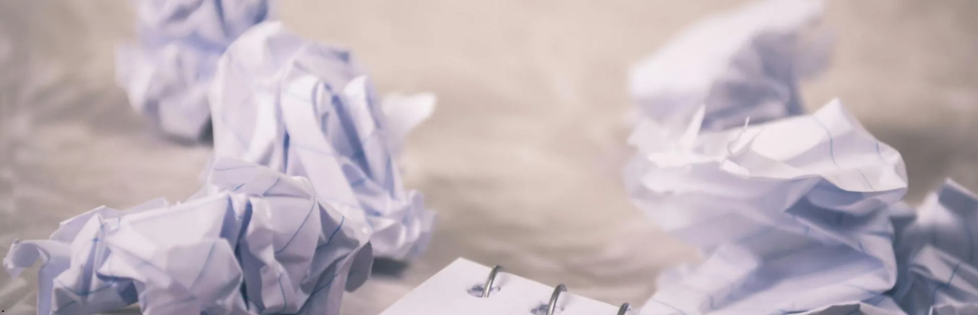 Scrunched up paper balls with a partially visible notepad on a textured surface.