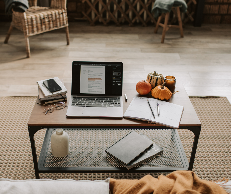 Laptop, notebook, pumpkins, and candles on coffee table in cozy living room.