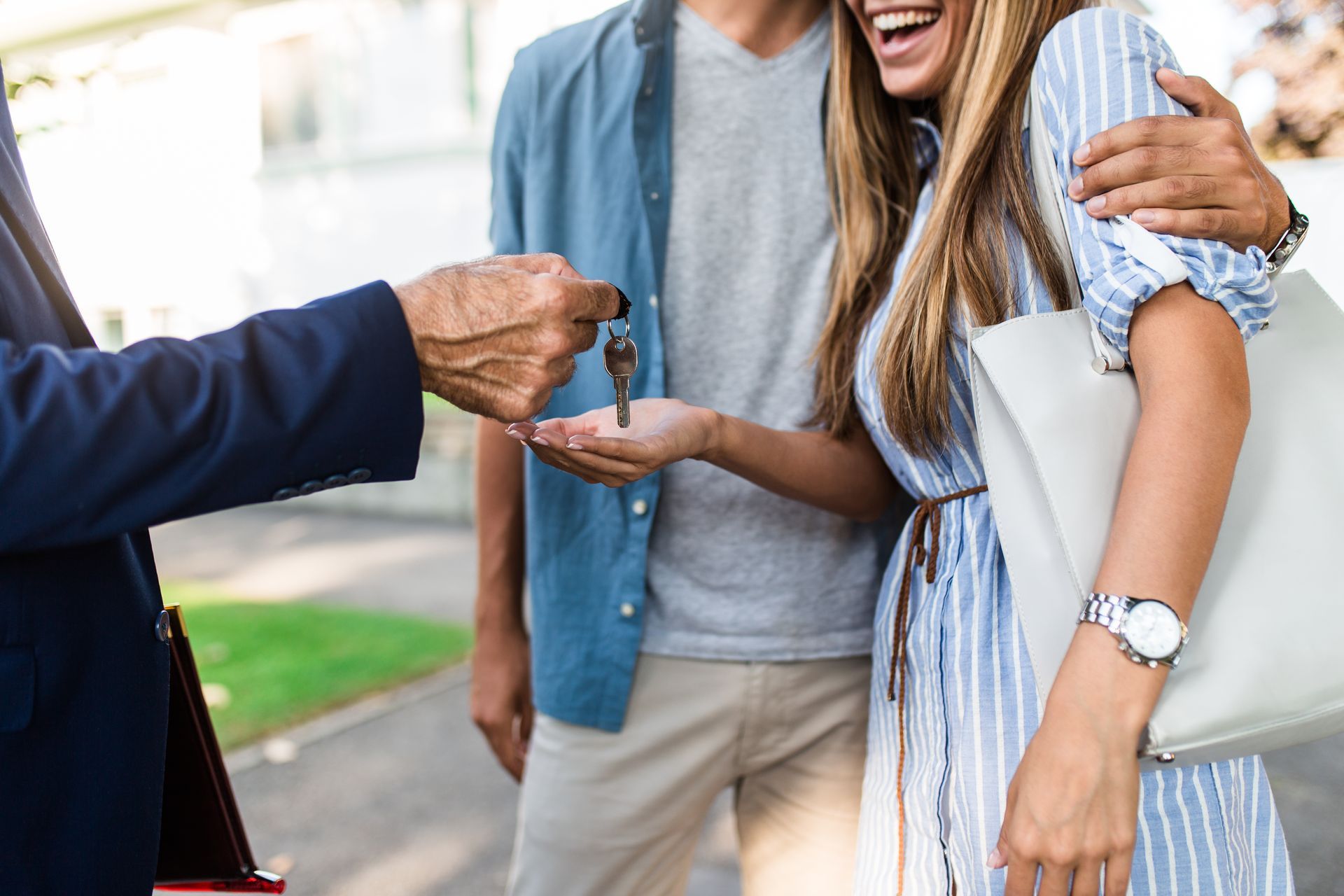 A person in a suit hands house keys to a smiling couple outdoors.