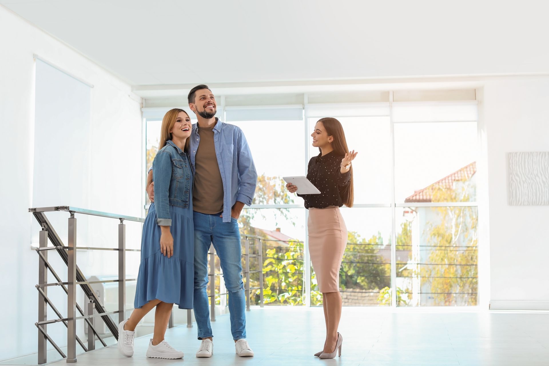Real estate agent showing a couple a bright, empty room with large windows.