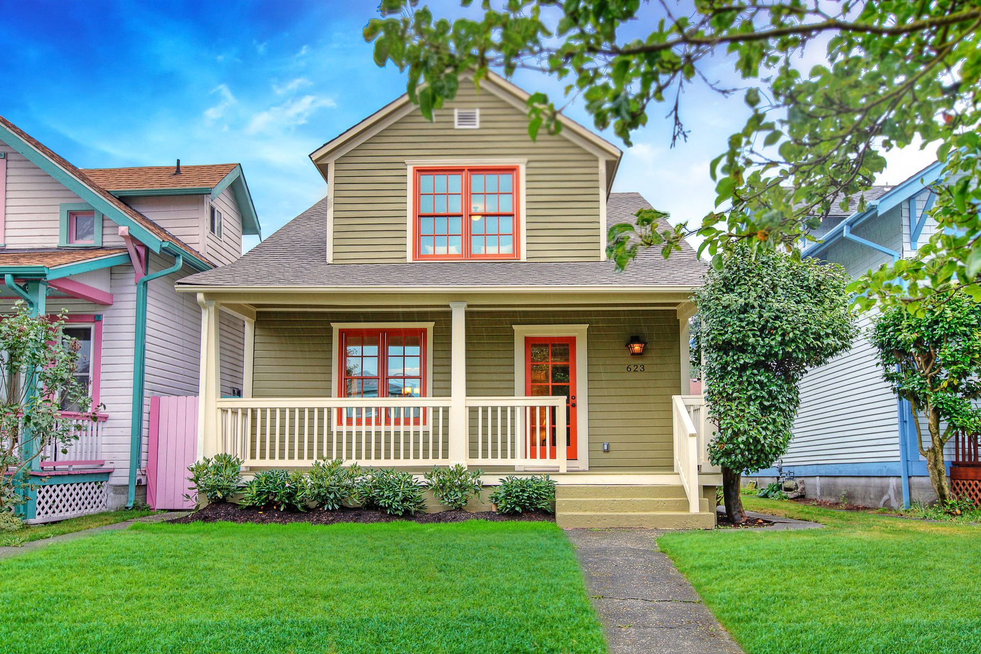 Two-story gray house with porch, lit windows, and manicured lawn. Dusk setting.