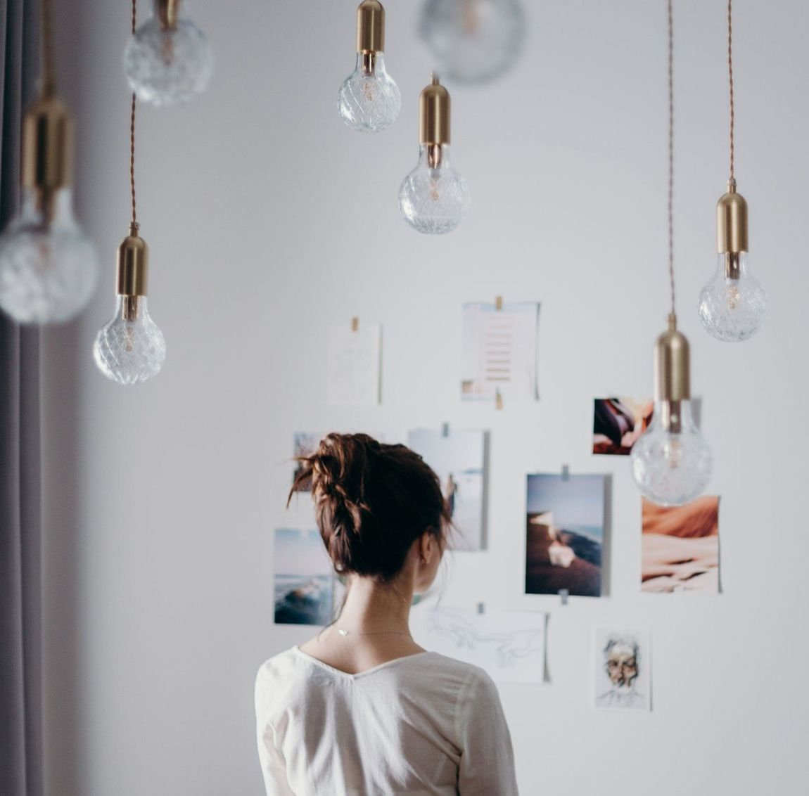 a girl looking at images on a white wall surrounded by ornate hanging lightbulbs symbolizing inspiration