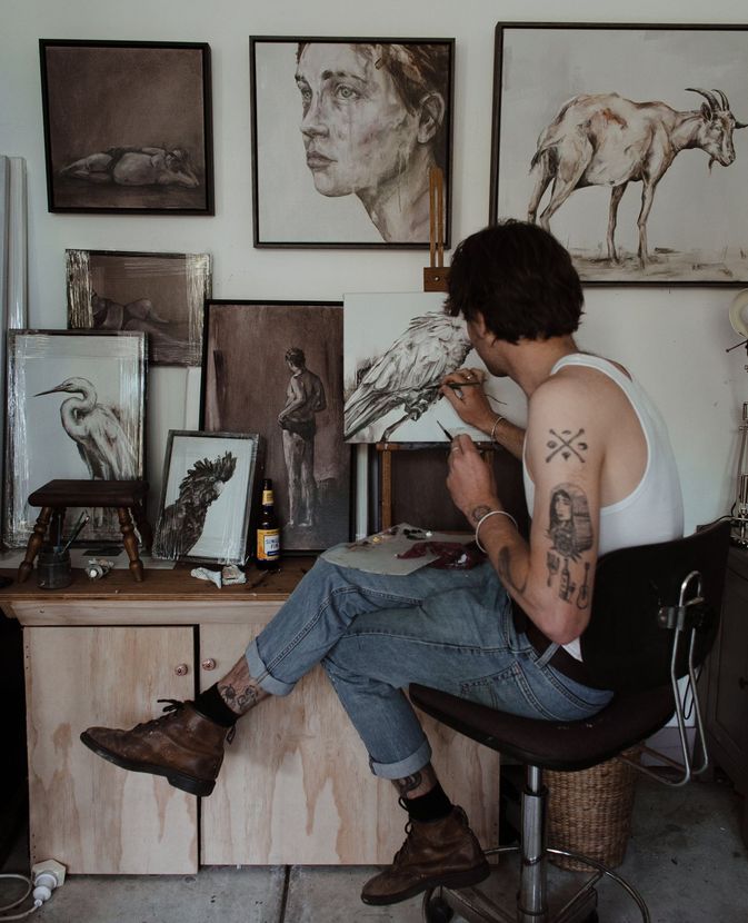 a tattooed artist working on his canvas surrounded by various pieces of art embodying the creative process