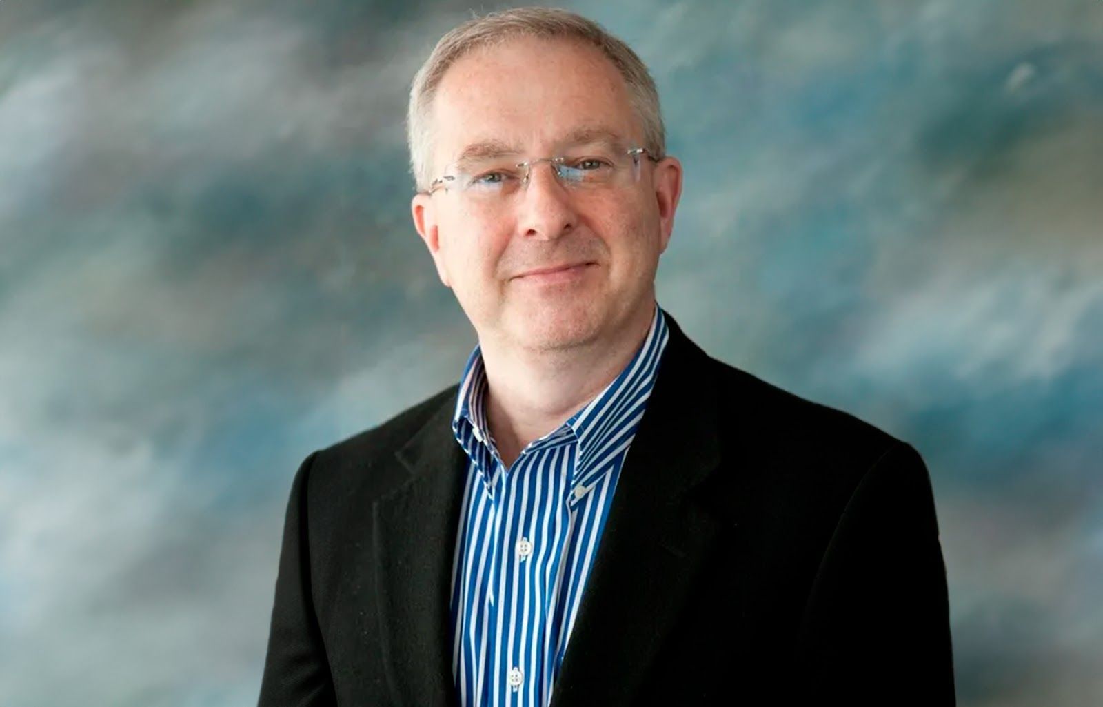 A man in a suit and striped shirt is smiling for the camera