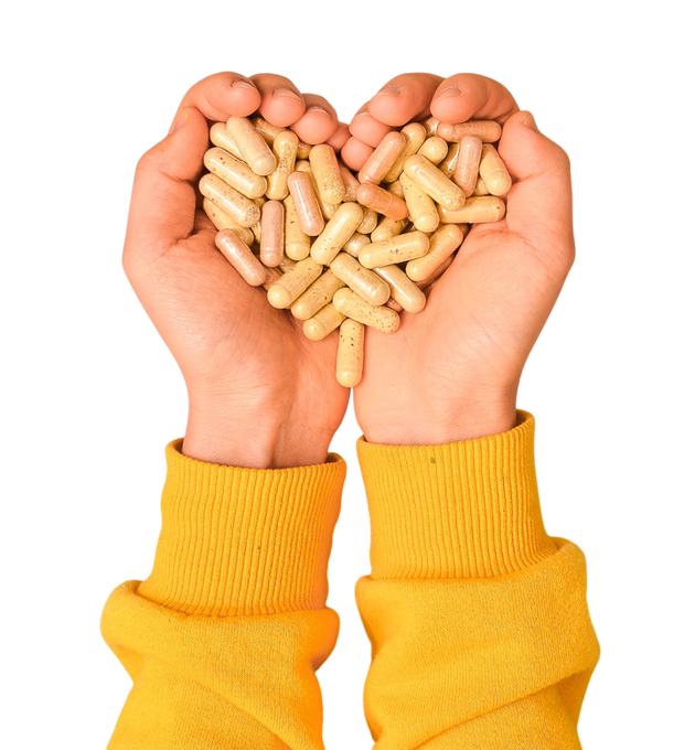 Manos con mangas amarillas que sostienen una forma de corazón hecha de cápsulas beige.