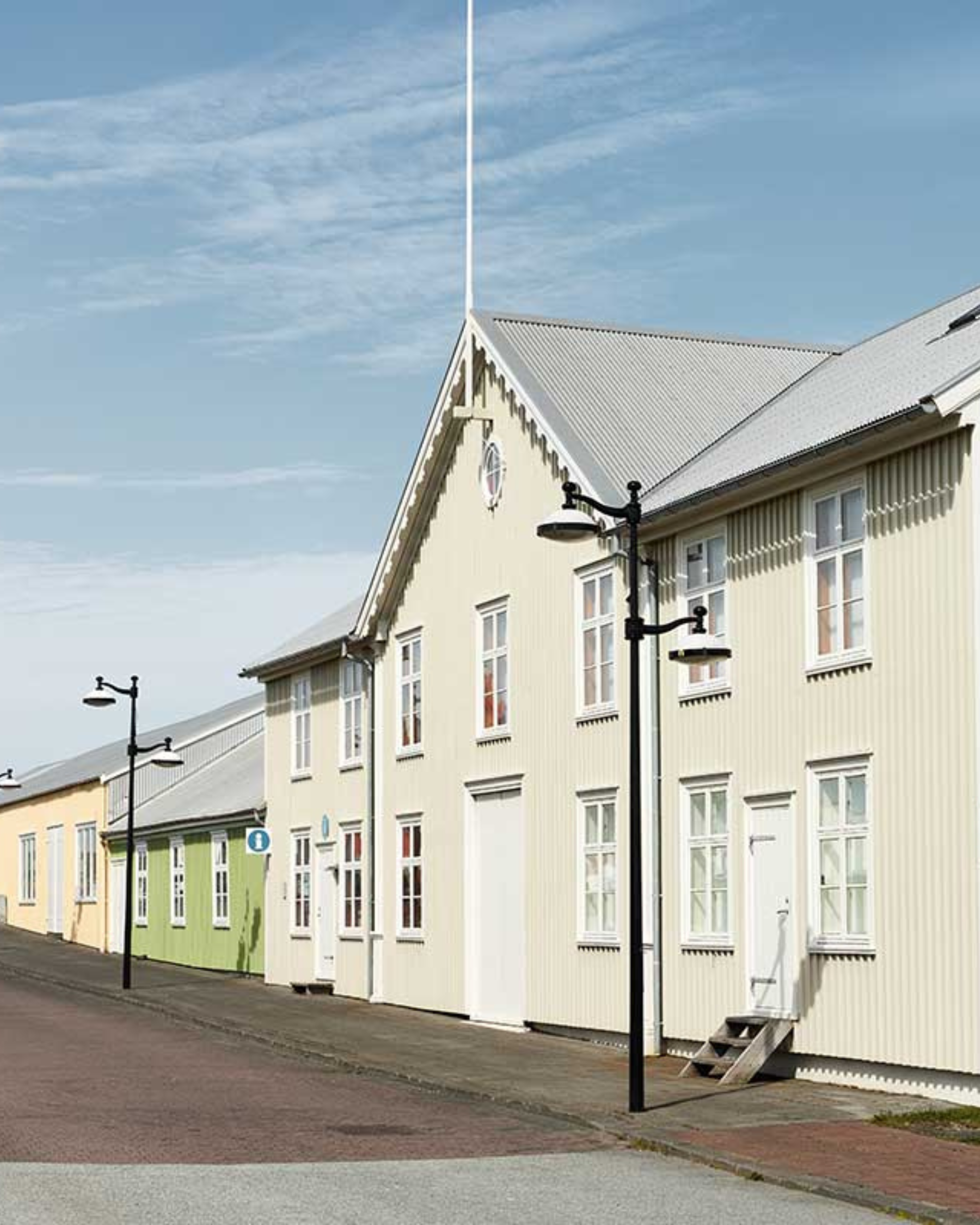 Röð af ljósum húsum meðfram malbikuðum götu undir bláum himni.