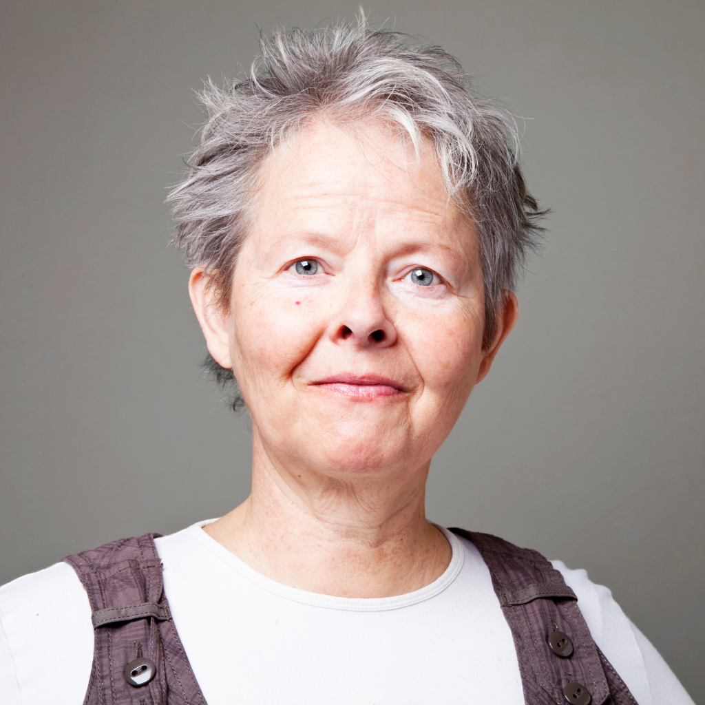 A woman with gray hair is wearing a white shirt and a purple vest.
