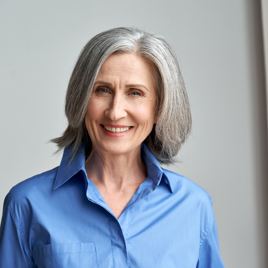 A woman with gray hair is wearing a blue shirt and smiling.