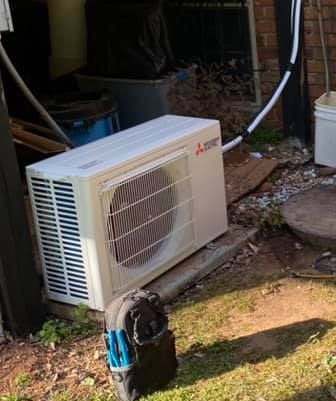A white air conditioner is sitting on the ground outside of a building.