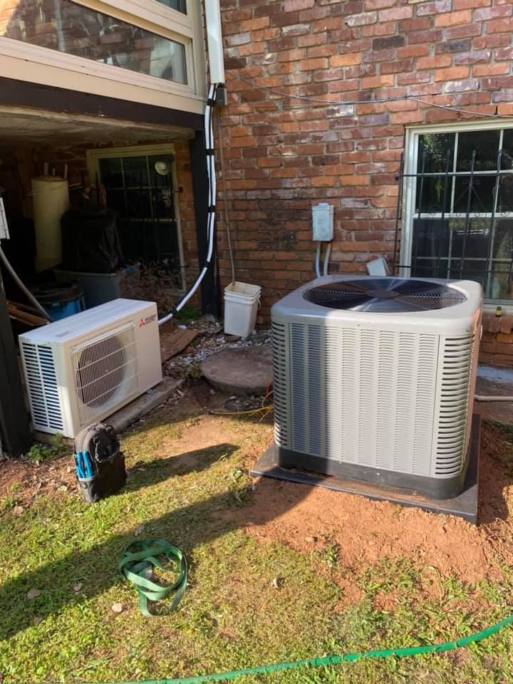 An air conditioner is sitting in the backyard of a brick house.