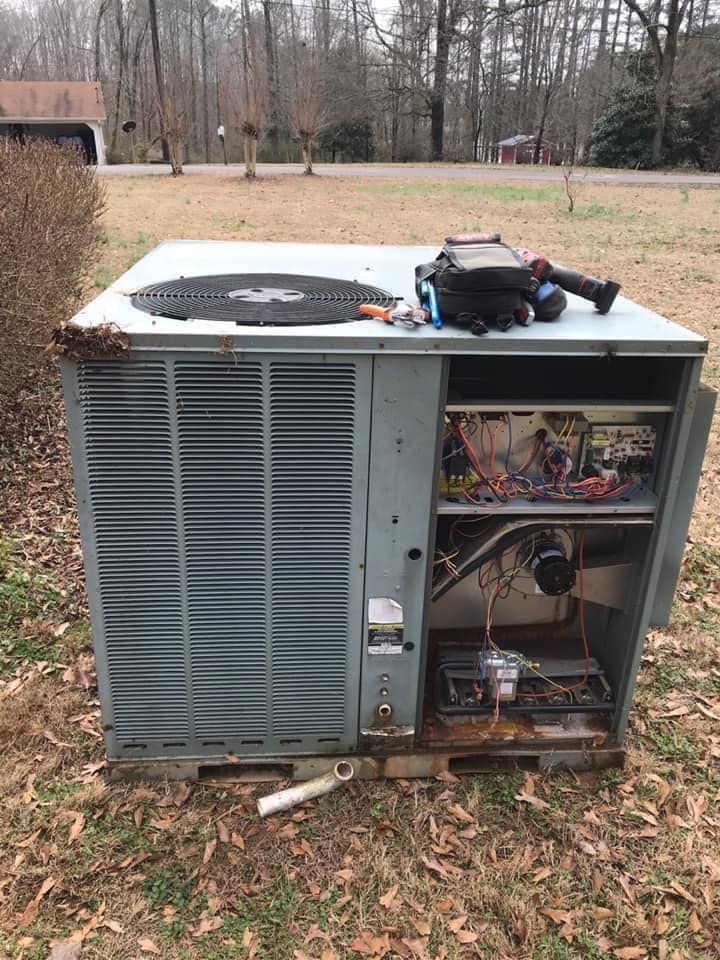 A broken air conditioner is sitting on top of a pile of leaves in a field.