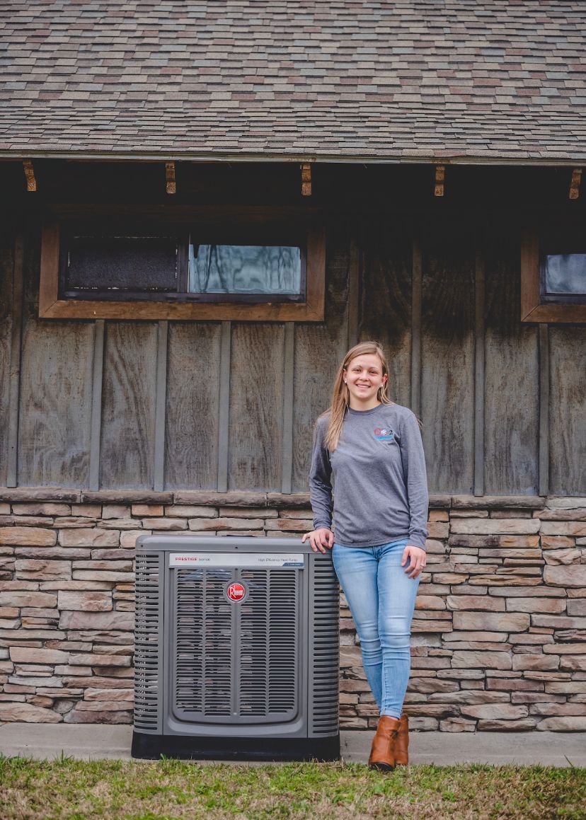 A woman is standing next to a large air conditioner in front of a stone building.