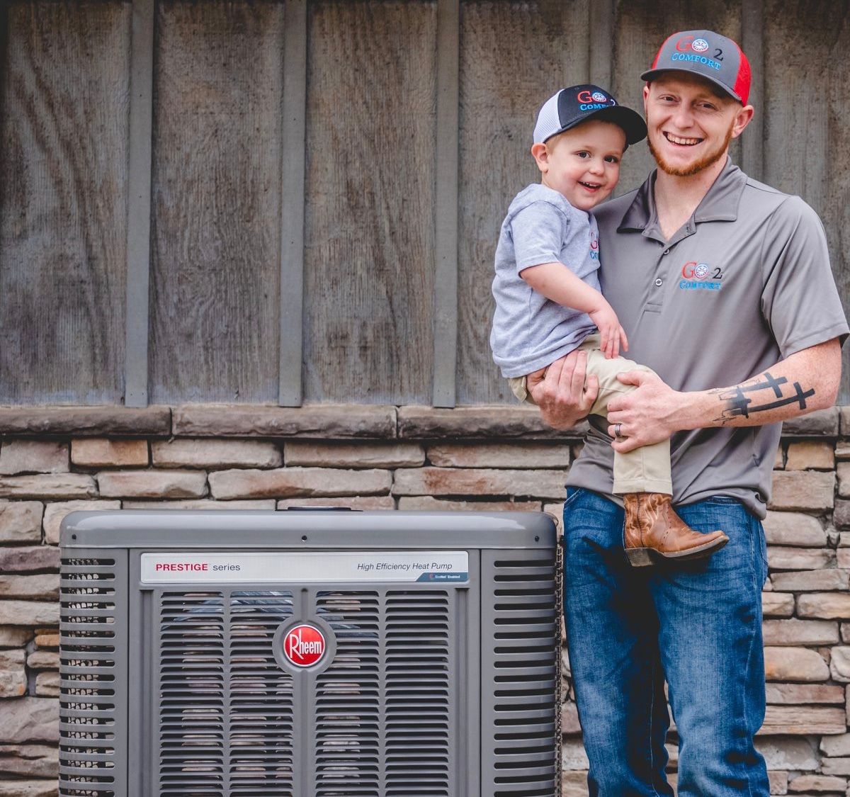 A man is holding a little boy in front of an air conditioner.