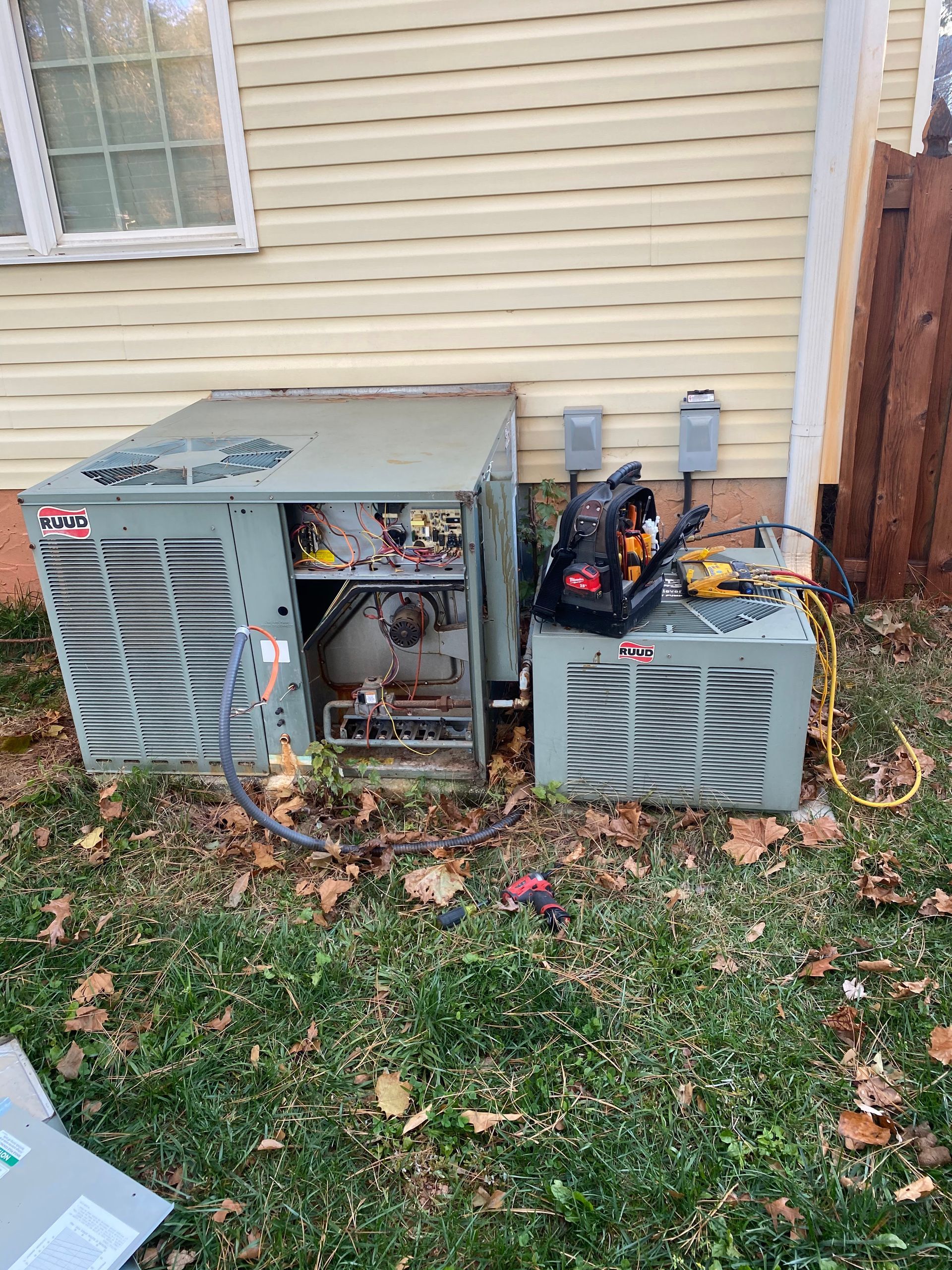 An air conditioner is sitting in the grass next to a house.