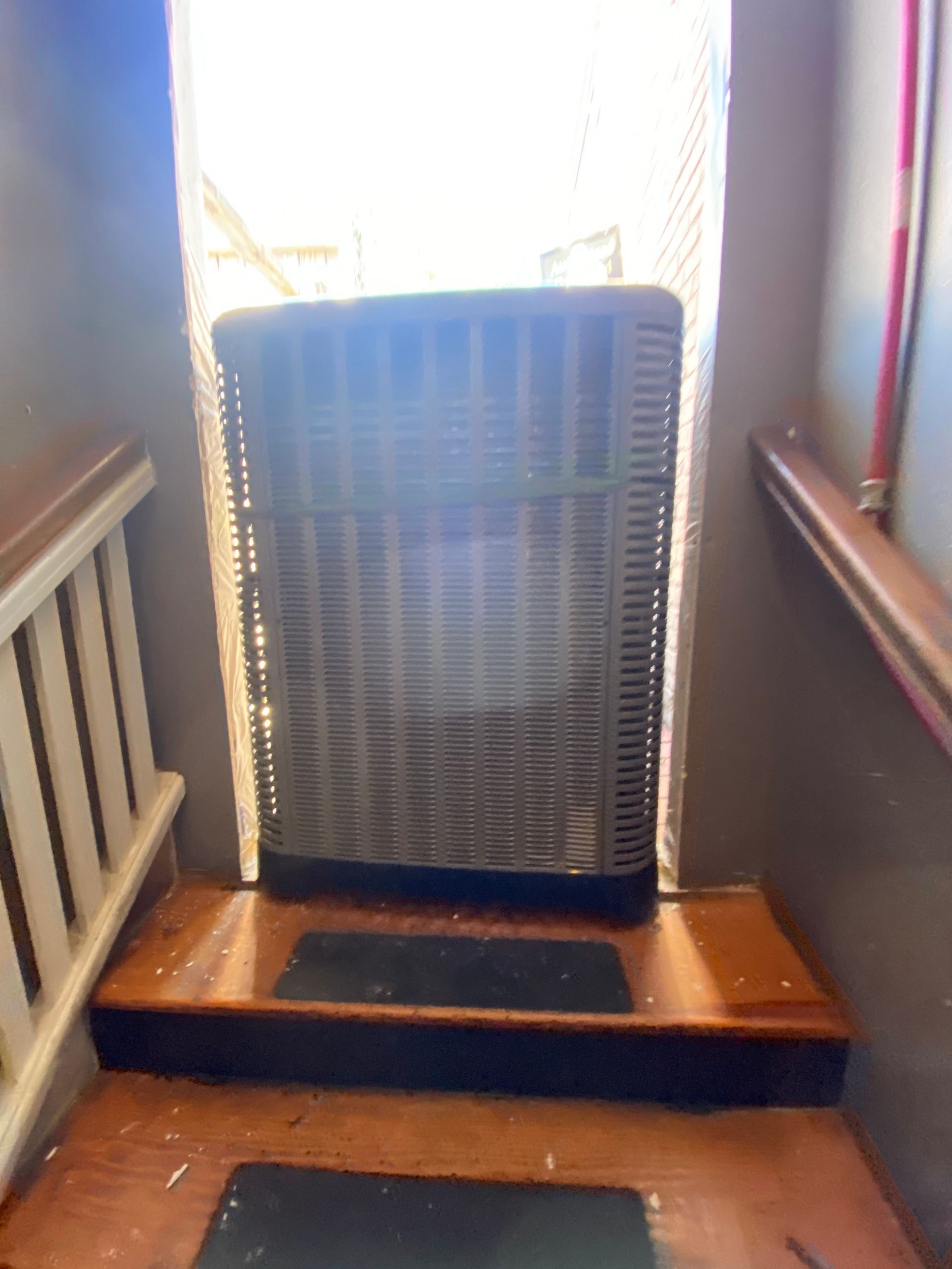 A fan is sitting on a wooden shelf next to a window.