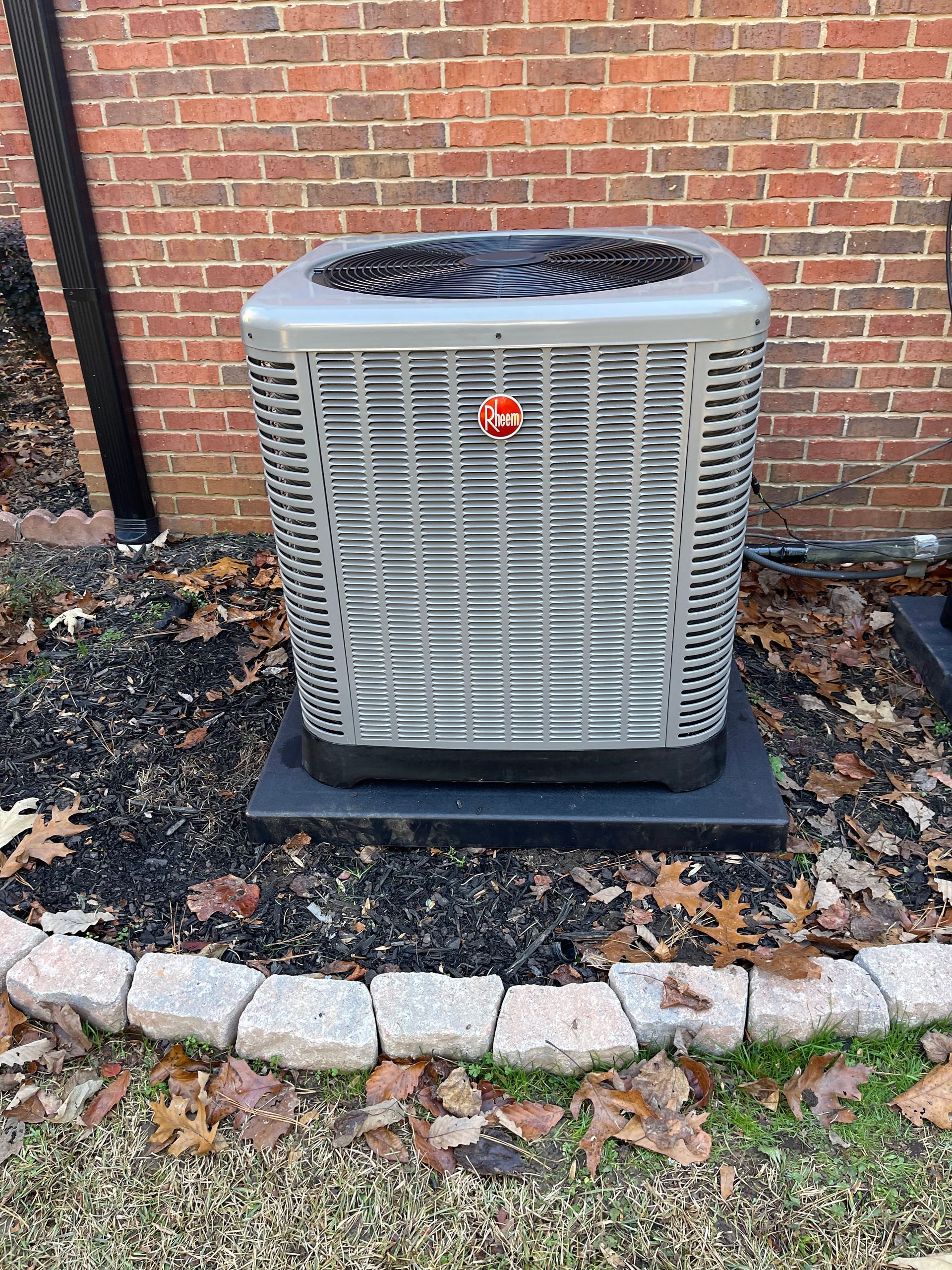 A large air conditioner is sitting in the grass in front of a brick building.