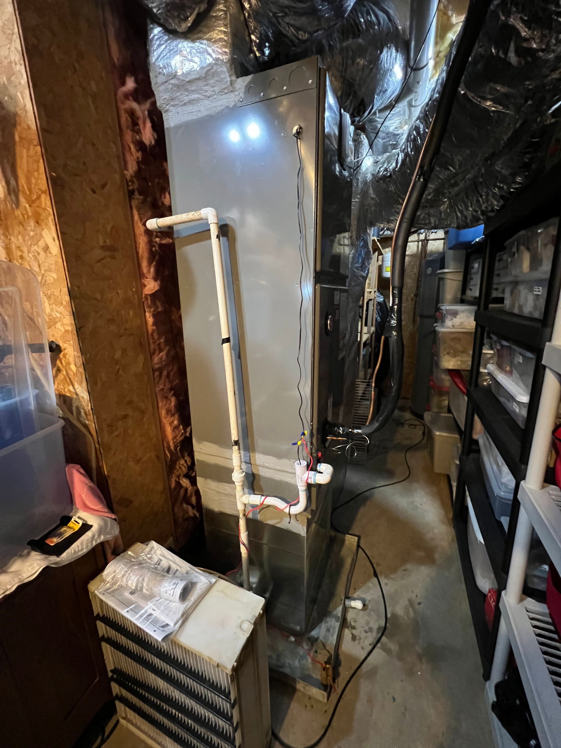 An air conditioner is sitting in a basement next to a ladder.