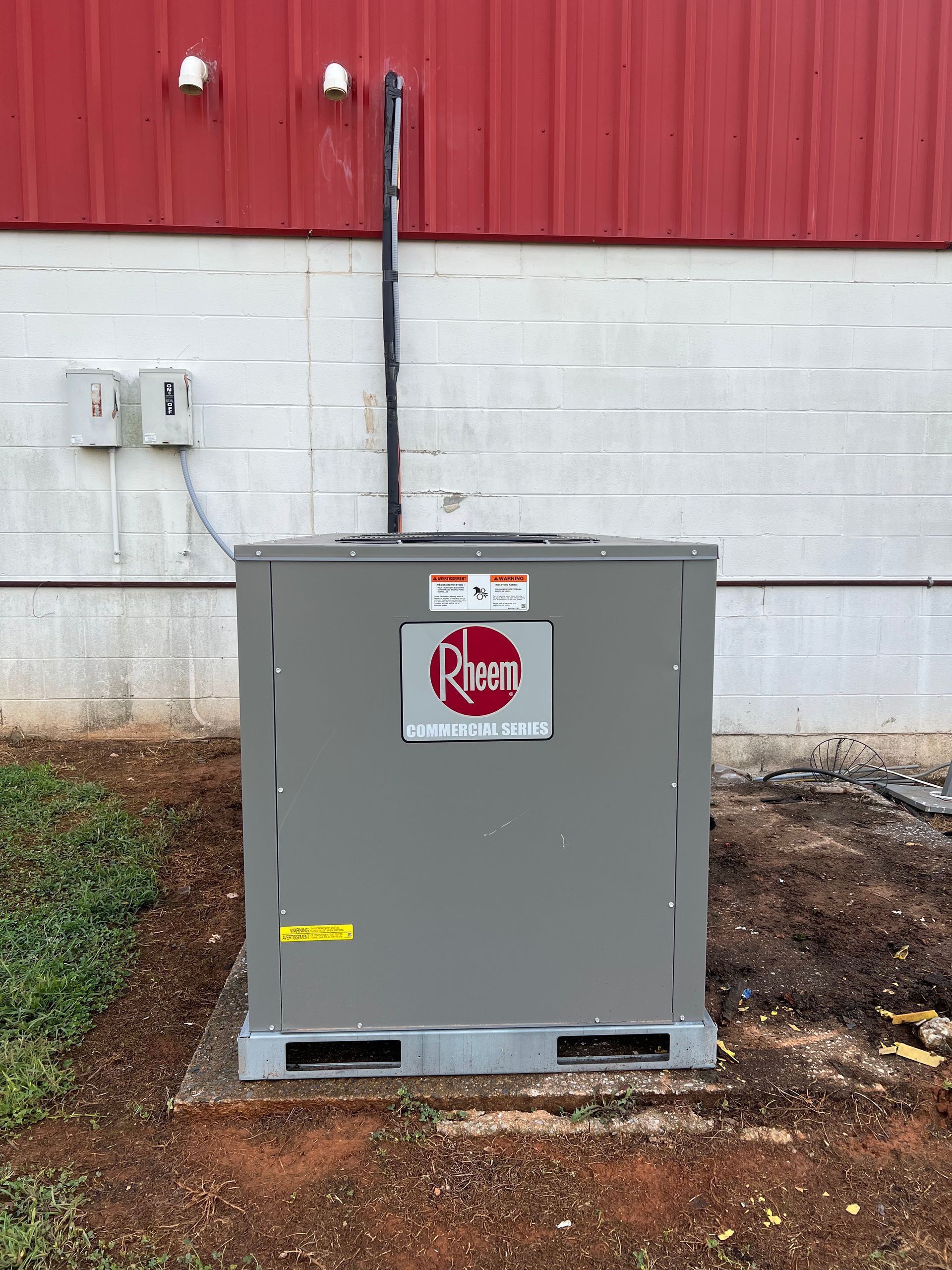 A rheem air conditioner is sitting outside of a building.