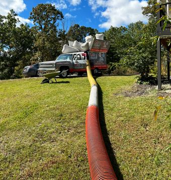 A truck is parked in a grassy field with a hose attached to it.