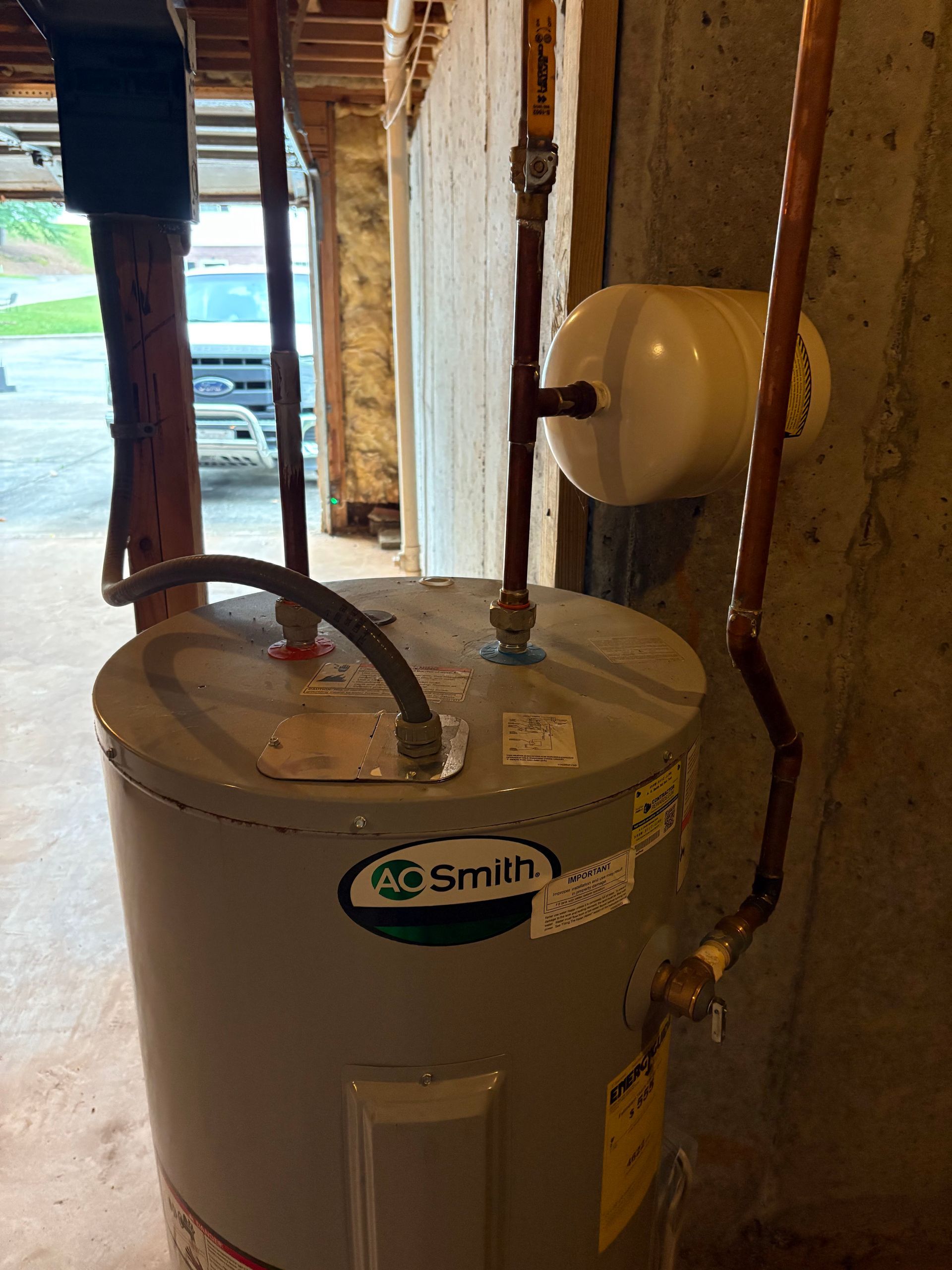 A water heater is sitting in a basement next to a wall.