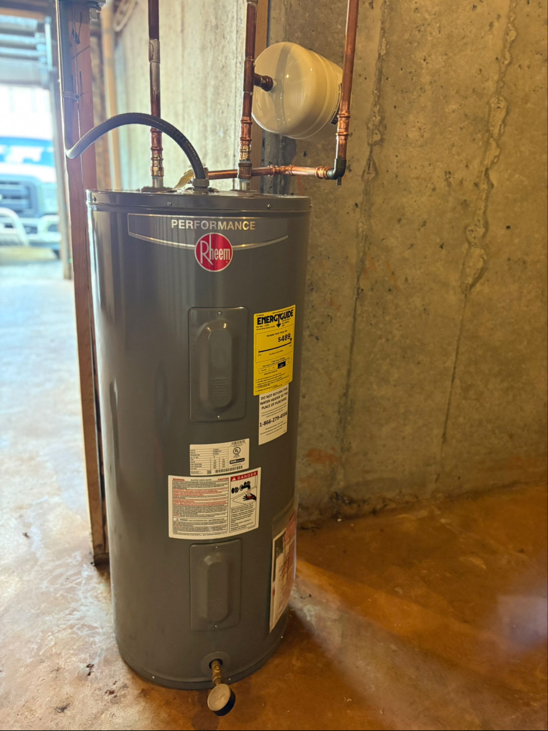 A water heater is sitting in a basement next to a wall.