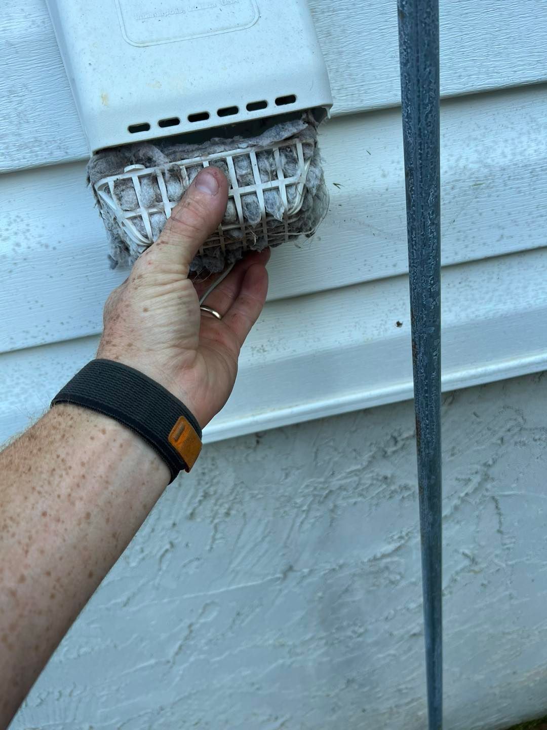 A person is cleaning a drain on the side of a house.