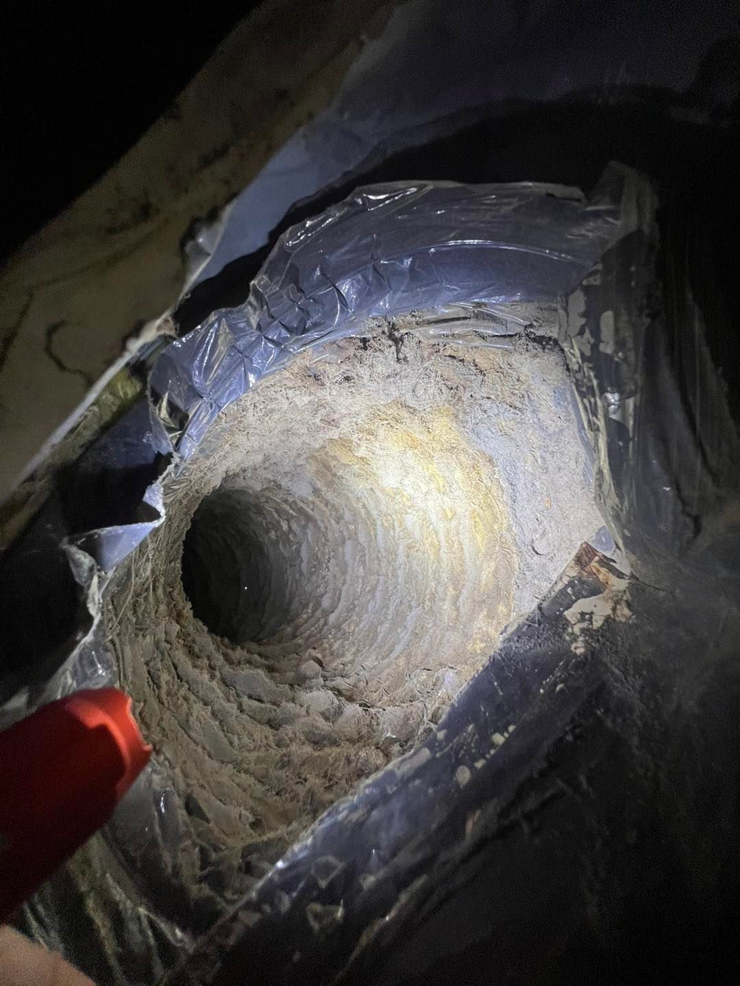 A person is holding a flashlight over a dirty exhaust pipe.