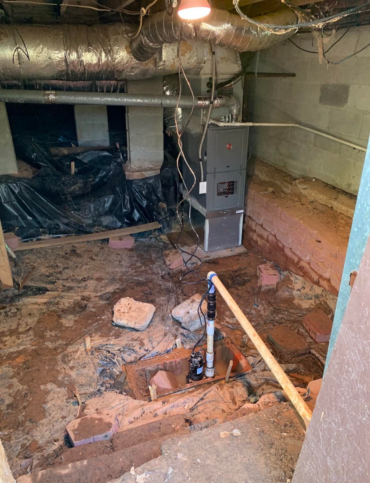 A dirty basement with a furnace and a shovel in it.