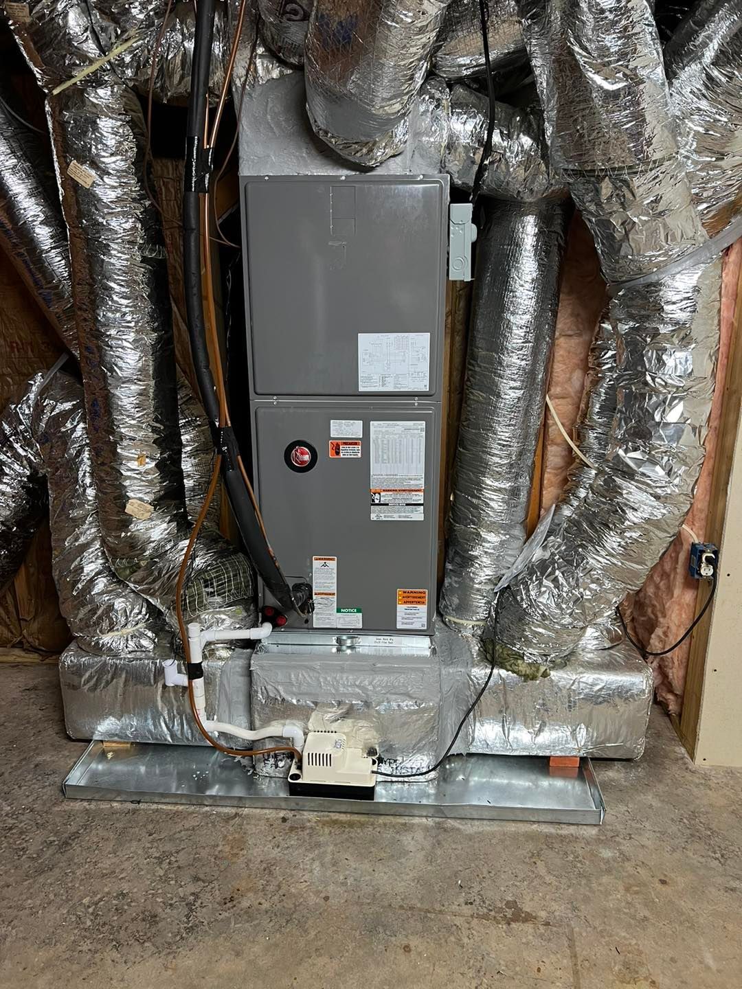 A large air conditioner is sitting in a basement next to a bunch of ducts.