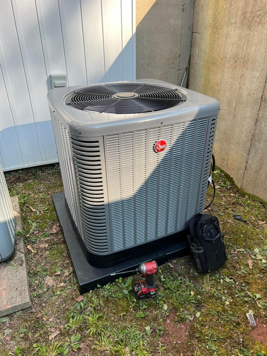 A gray and white air conditioner is sitting on the ground next to a drill.